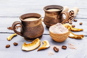 A picture of two jar mugs with brewed coffee of Excalix Mushroom Coffee, as well as chaga mushroom bark, coffee beans and ground lion's mane mushroom powder.